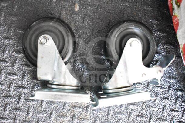 Two black caster wheels with metal brackets on a textured black surface.