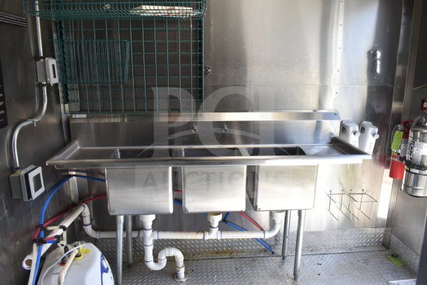 2021 Diamond Cargo food trailer interior showing a stainless steel triple sink with plumbing, fire extinguisher, and storage racks.