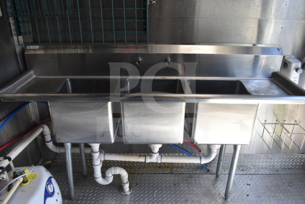 Triple stainless steel sink in 2021 Diamond Cargo food trailer, featuring plumbing setup and metal backsplash, great condition.