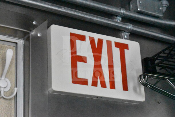 EXIT sign mounted on an interior wall with visible metal conduit and shelving nearby.