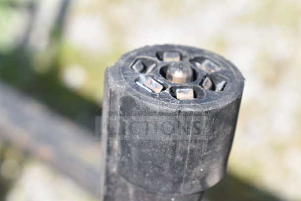 Close-up of a black, cylindrical component, possibly a trailer hitch part, showing metal connectors and a central bolt.