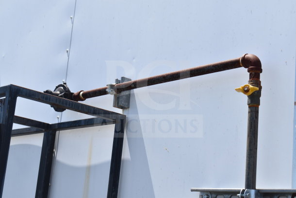 Rusty outdoor metal pipe installation with brackets against a white wall, featuring a yellow valve handle.