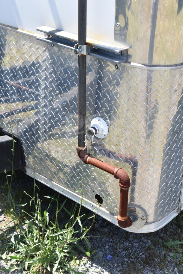Diamond Cargo 8.5x24 food trailer exterior with metal diamond-plate siding, pipe fittings, and visible ground vegetation.