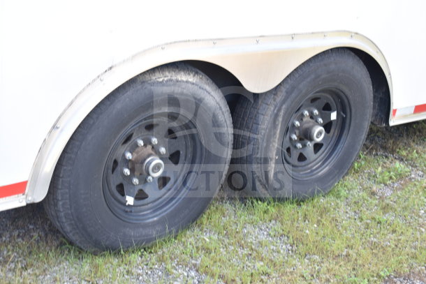 Black wheels of a 2021 Diamond Cargo 8.5x24 food trailer, dual axle, on grass and gravel surface.