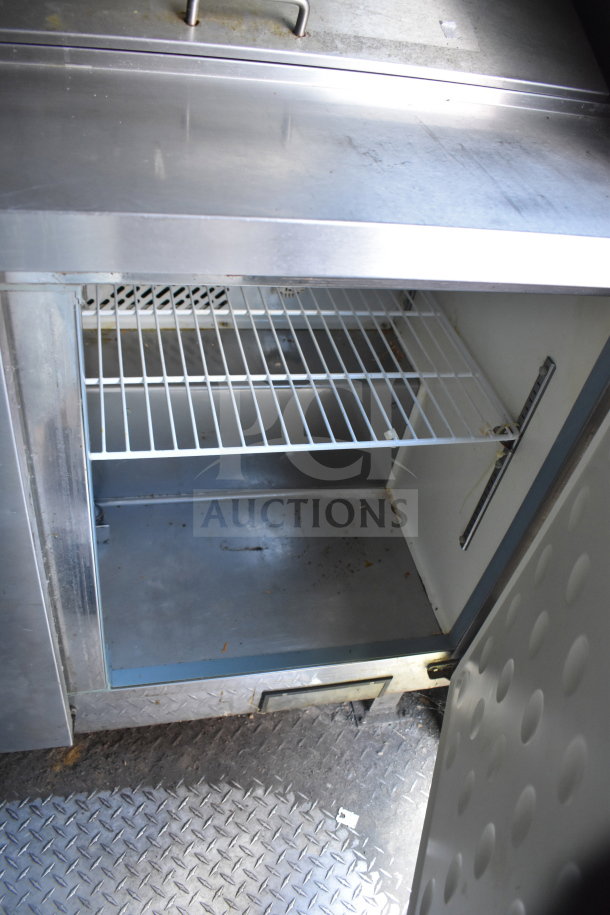 Interior view of a 2020 Diamond Cargo 8.5x24 food trailer undercounter fridge with wire shelving in used condition.