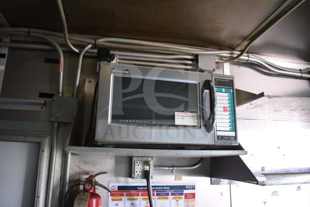 Sharp commercial microwave inside 2020 Diamond Cargo food trailer, featuring grease hood and fryer, with wiring and fire extinguisher visible.