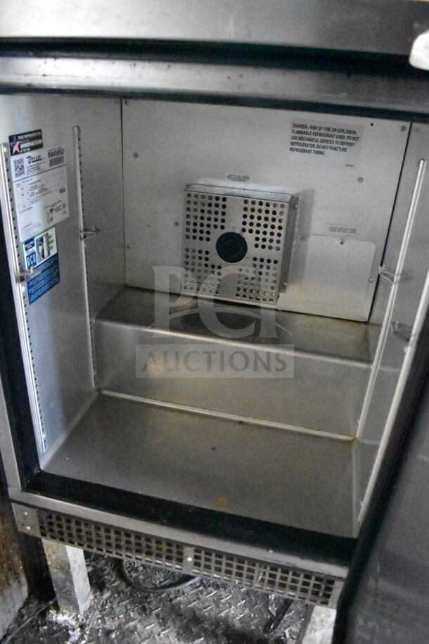 Interior view of the 2020 Diamond Cargo food trailer's refrigeration unit. Features include a warning label and industrial shelving.