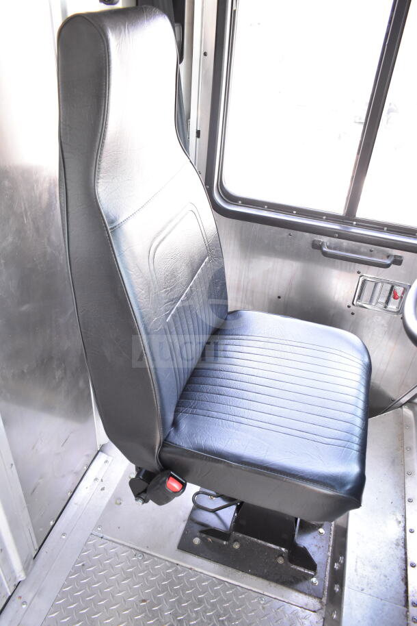 Driver seat of a 2020 Ford F59 food truck, featuring black upholstery and metal flooring, shown in good condition.