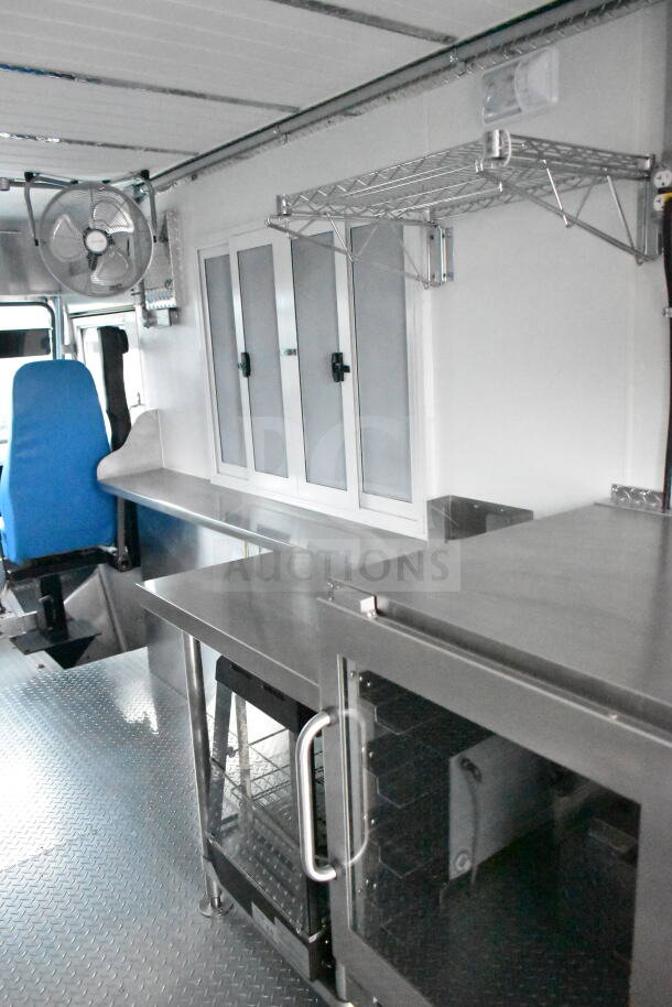 Interior of a 1993 GMC Step Van showcasing stainless steel surfaces, shelving, fan, and a blue seat, highlighting its clean condition.