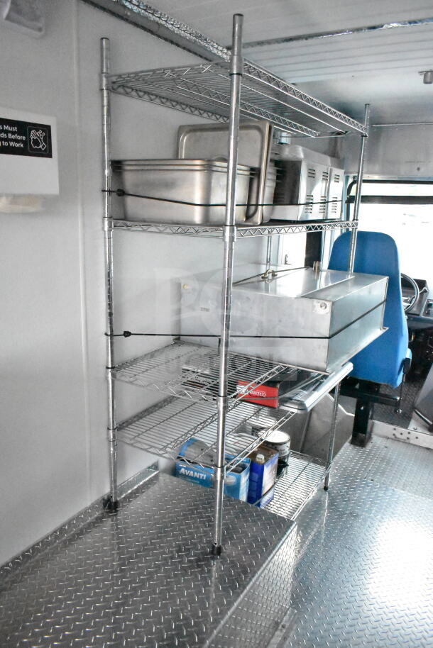 Interior of a 1993 GMC Step Van showing metal shelving with storage containers, diamond plate flooring, and a driver’s seat.
