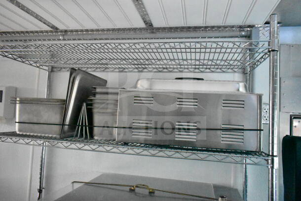 Stainless steel trays and pans stacked on a wire shelf inside a vehicle, possibly indicating a kitchen setup.