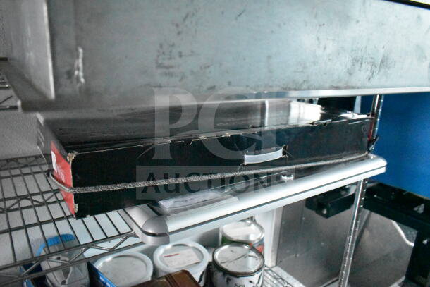 A shelf in a 1993 GMC Step Van showing black cardboard boxes with scuffs, metal casing, and various items below.