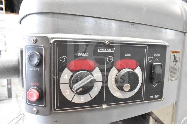 Hobart Legacy HL600 commercial dough mixer control panel, showing start/stop buttons, speed and time dials, and warning label.