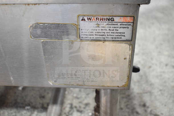 Commercial floor-style braising pan with warning label. Shows signs of wear; sturdy construction, ideal for large-scale cooking.