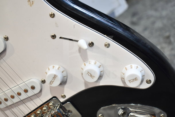 Close-up of a Rock Jam guitar control panel featuring volume and tone knobs, selector switch, and white pickguard.