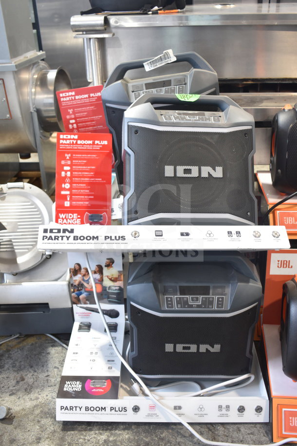 4 Ion Party Boom Plus speakers in a store display, featuring robust design, wireless Bluetooth, multi-colored lights, and microphone compatibility.