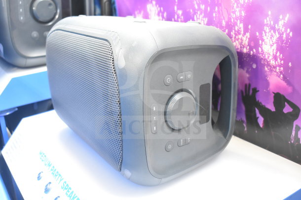 Onn Medium Party Speaker display, black with silver grille, control knobs, and buttons visible, shows vibrant display in background.