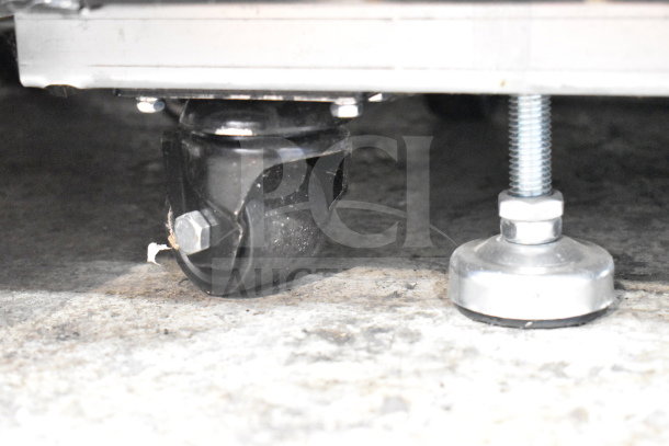 Bottom view of a Migali C-10RM-HC cooler showing a commercial caster and adjustable foot, highlighting mobility features.