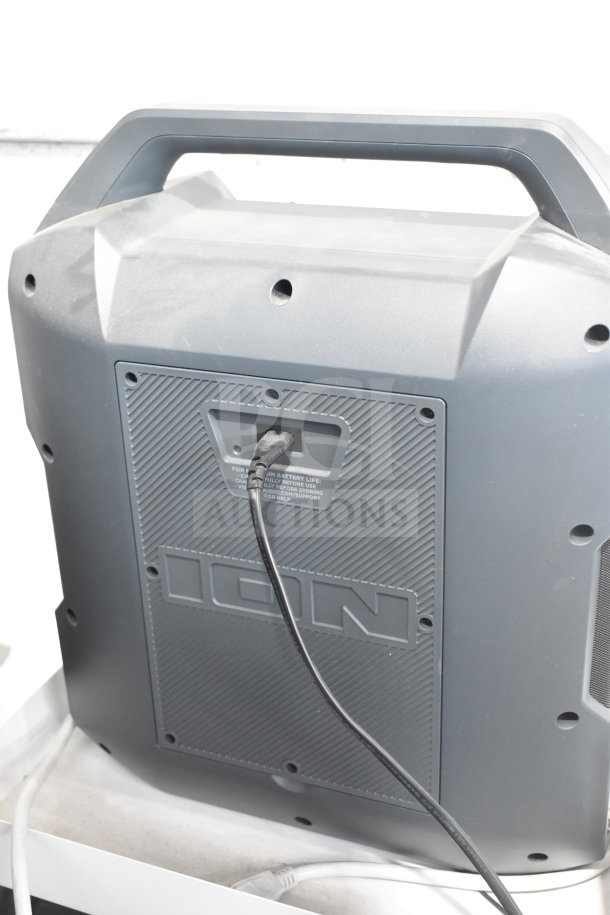 Ion portable speaker, gray, store display, rear view with power cable plugged in, textured panel, brand label visible.