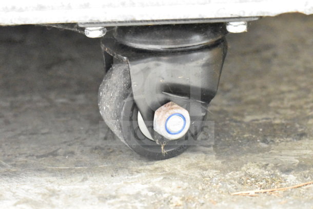 Commercial caster wheel of Migali C-72FM-HC freezer, black with a bolt, on a concrete floor.