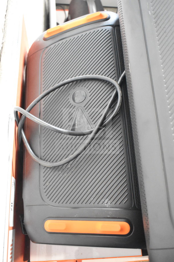 JBL speaker with textured design, orange accents, and visible power cord, part of store display. Condition appears used.