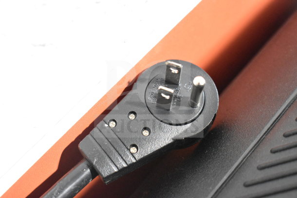 Close-up of an electrical plug near an orange and black surface, possibly part of the 2 Store Display with JBL Speaker auction item.
