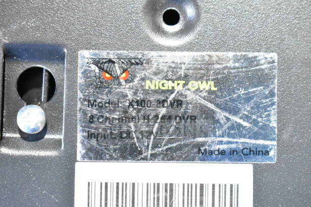 Close-up of Night Owl X100 DVR label showing model number, 8 channel H.264 DVR details, input DC 12V, scratched condition.