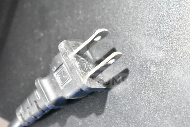 Close-up of a two-prong electrical plug on a textured surface, part of a 15-item electronics auction lot.