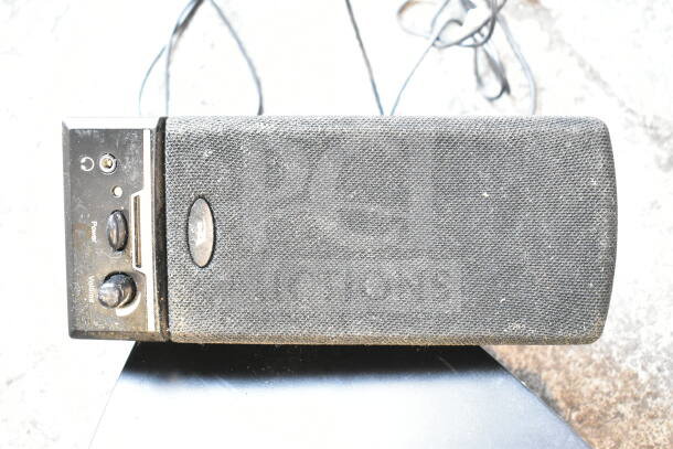 Dusty speaker with power and volume knobs, worn fabric cover, and visible cables. Part of a mixed electronics lot.