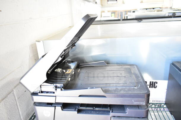 HP LaserJet Pro MFO M127fn printer on a countertop, lid open, shows moderate wear. HP logo visible.