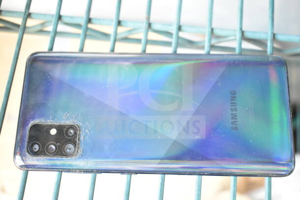 Samsung smartphone with holographic back, quad camera setup. Visible smudges and dust. Brand logo on the back.