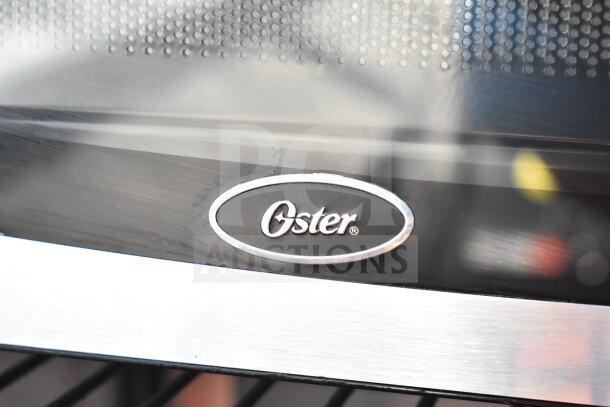 Oster OGYU701 Countertop Microwave Oven, 120V. Features stainless steel design, clear front panel with Oster logo.