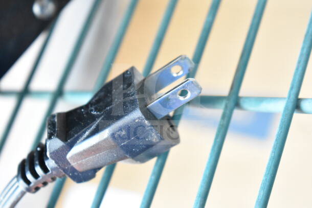 Close-up of a black electrical plug, likely for the Oster OGYU701 Microwave, resting on a metal surface.