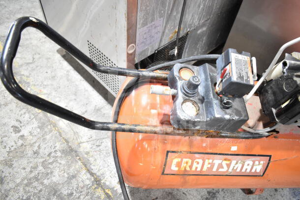Craftsman air compressor, orange tank, visible wear. Features two pressure gauges, control knob, and Craftsman branding.