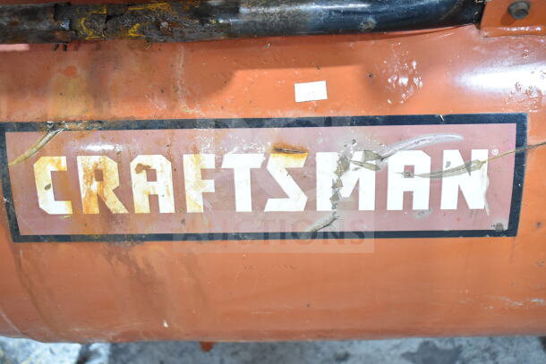 Craftsman air compressor with visible wear and rust, featuring a prominent Craftsman logo on an orange surface.
