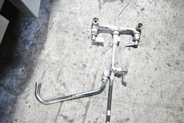 Chrome faucet with spray nozzle attachment, dual handles, vintage condition, visible wear and patina.