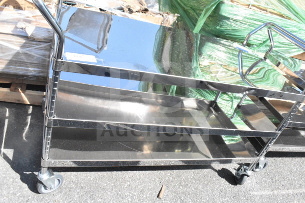 3 Tier metal utility cart with commercial casters, reflective finish, three shelves, signs of light wear, ideal for storage or transport.