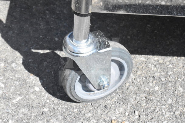 Commercial caster wheel of 3-tier cart, metal frame, on outdoor surface, in good condition.