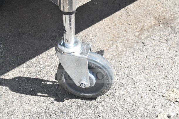 Commercial caster wheel of a 2-tier or 3-tier cart, durable metal frame, on concrete surface, part of auction.