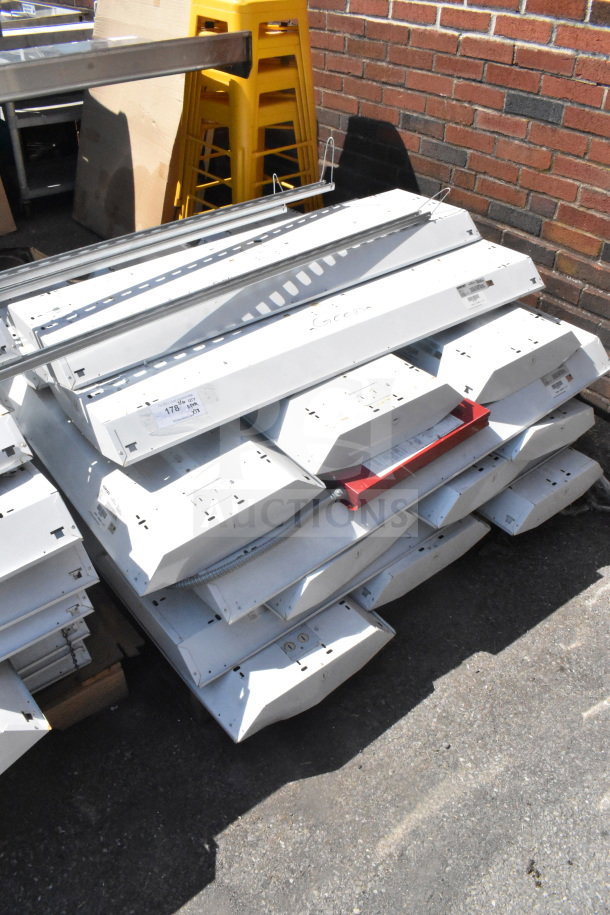 Howard HFA3E654APSMV light fixtures, stack of 18, 120-277 volts, used condition. Visible labels and industrial setting.
