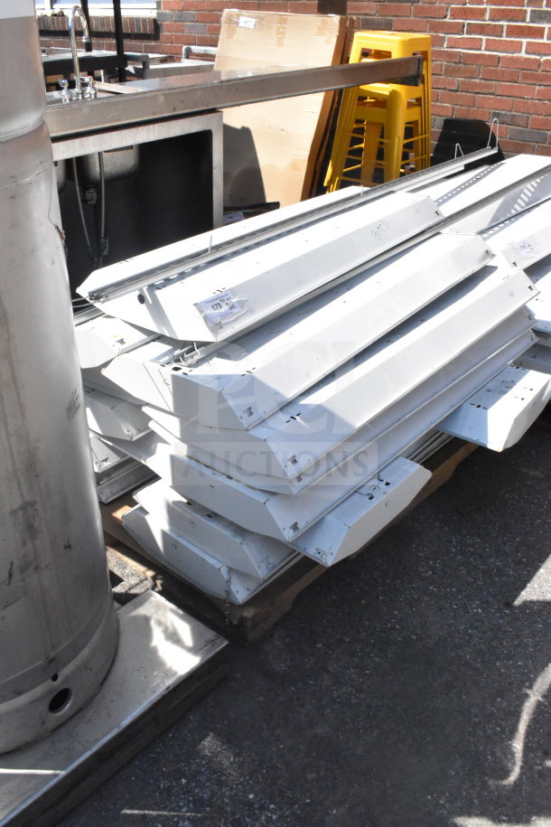 Stack of 12 Howard HFA3E654APSMV light fixtures, 120-277 volts. Good condition, metal housing, auction lot number visible.