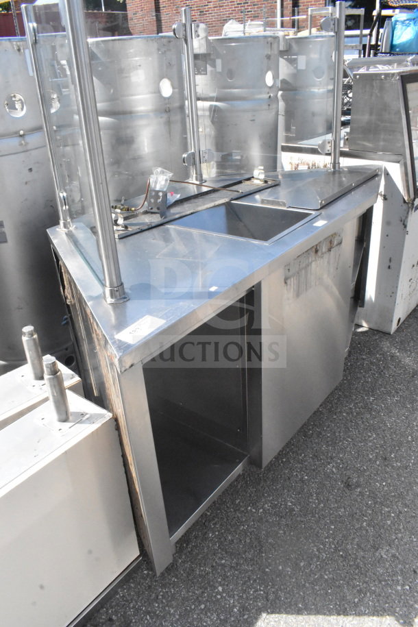 Stainless steel counter with bay and sneeze guard, featuring open storage space below. Some visible wear and rust present.
