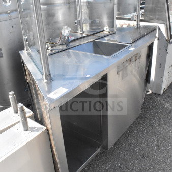 Stainless steel counter with bay and sneeze guard, featuring open storage space below. Some visible wear and rust present.