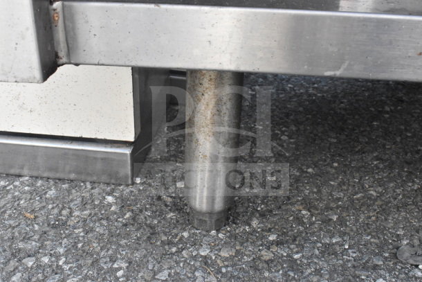 Stainless steel counter with bay and sneeze guard, showing minor rust and wear on the legs, ideal for food service.