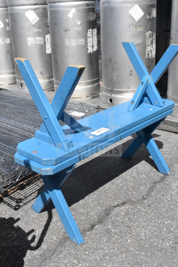 Blue wooden bench with X-shaped legs, showing minor wear. Auction label attached, offering two units per bid.
