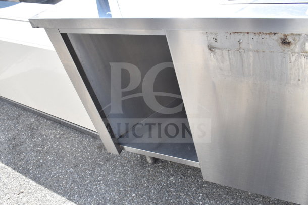 Stainless steel counter with an integrated bay and sneeze guard, showing surface wear and discoloration.