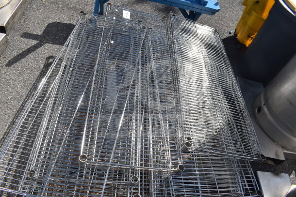 Lot of 18 chrome finish wire shelves stacked on pavement, in good condition, showcasing open-wire construction and reflective surface.