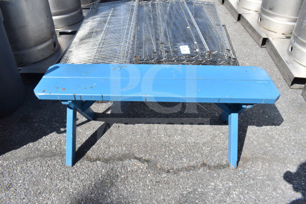 Blue wooden bench with signs of wear, visible scratches. Simple, sturdy construction. Ideal for outdoor use.