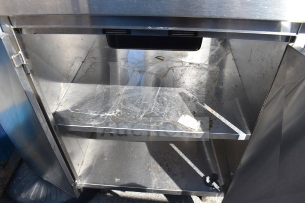 Commercial stainless steel counter with four doors, shows signs of wear, featuring interior shelves. Ideal for restaurant use.