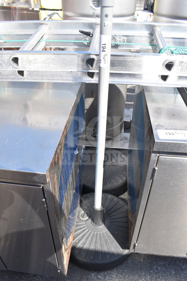 Two round, black umbrella bases in used condition, designed for stability. Tags indicate lot and quantity numbers.